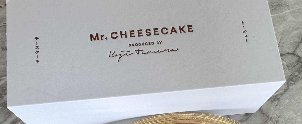 ミスターチーズケーキの白い化粧箱のふた。茶色の文字でMr. CHEESECAKE PRODUCED BYとサイン、両端に縦書きでチーズケーキとトーキョー