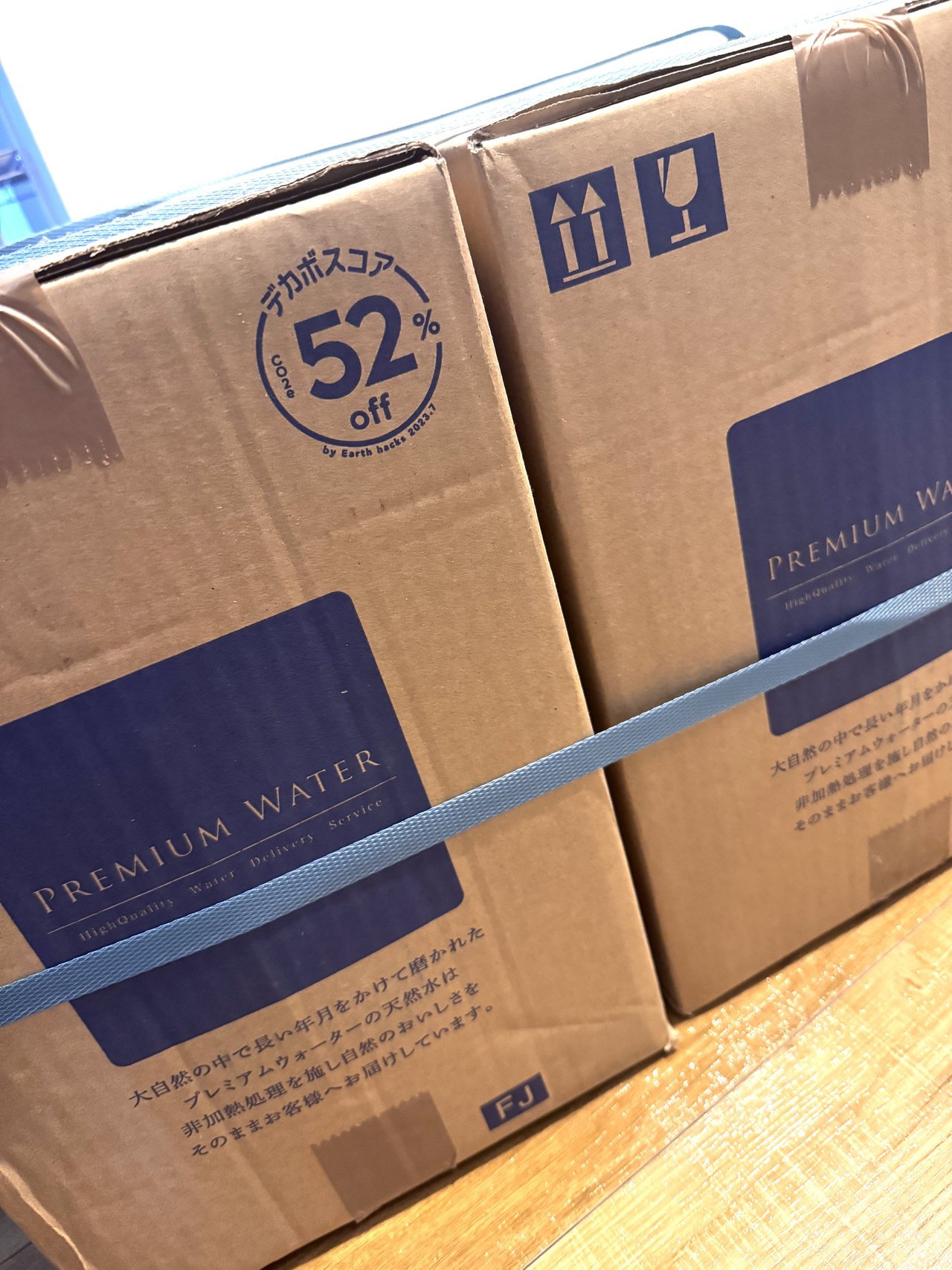 PREMIUM WATERと印刷された段ボール2箱が青いバンドでまとめられ木の床に置かれている