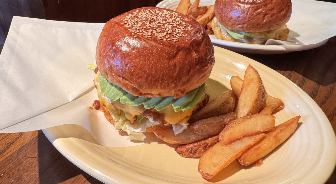 紙を敷いた楕円の皿にのったハンバーガーと皮付きの太いポテト。奥にもう1つのバーガー