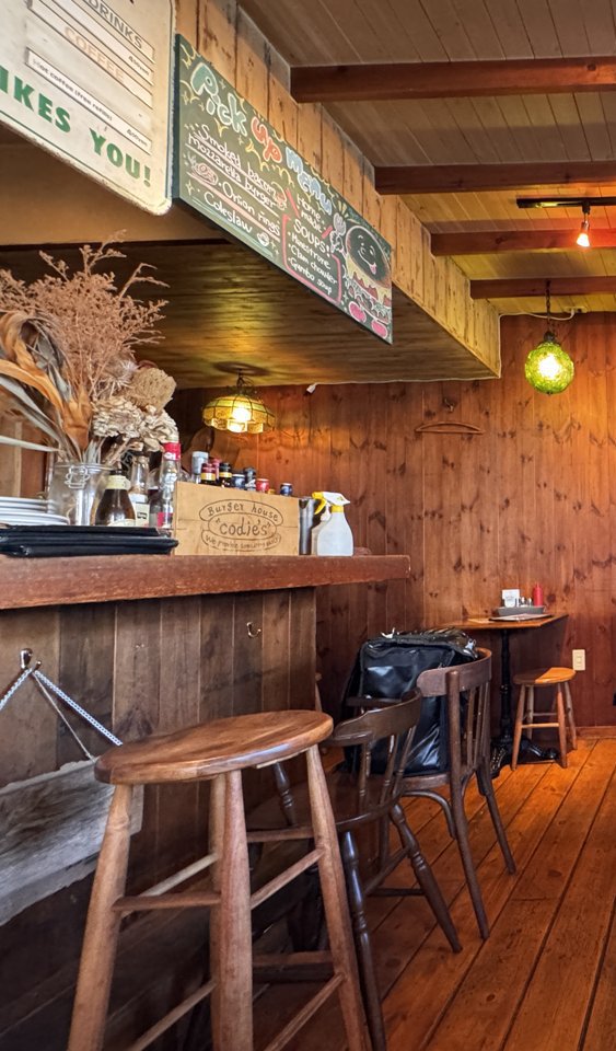 コーディーズの店内。木のカウンターと丸いスツール、天井の梁と緑のガラスのランプ