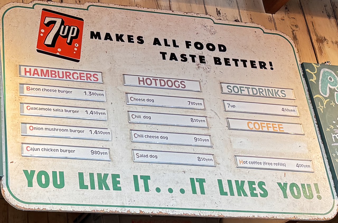 7upの看板のメニュー。HAMBURGERS・HOTDOGS・SOFTDRINKS・COFFEEの欄に値段が並ぶ