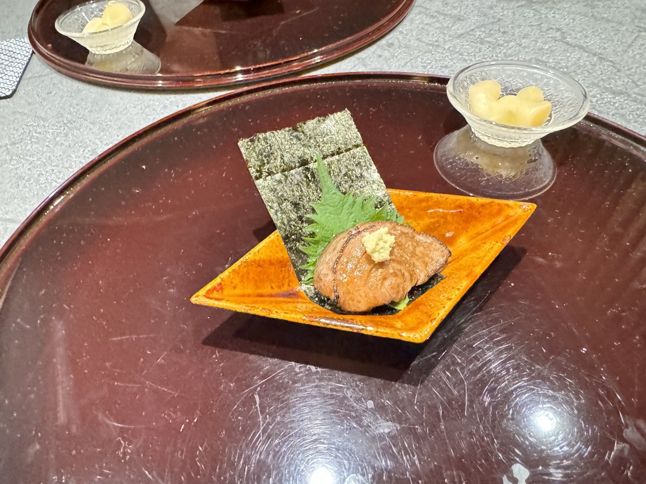 オレンジ色の角皿に海苔と大葉、炙った具にわさびをのせた一品