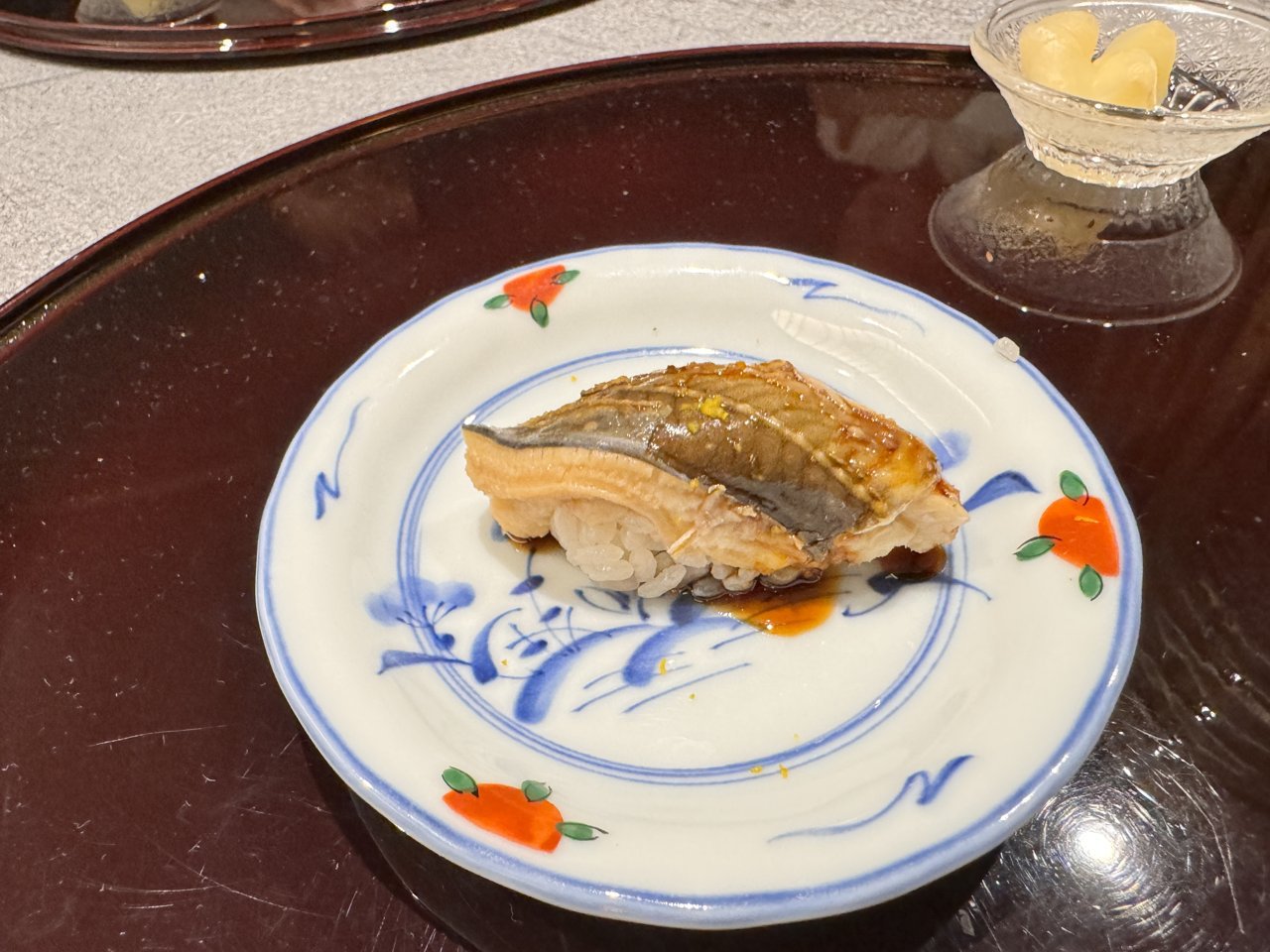 染付の丸い皿にのったたれをかけた穴子のにぎり