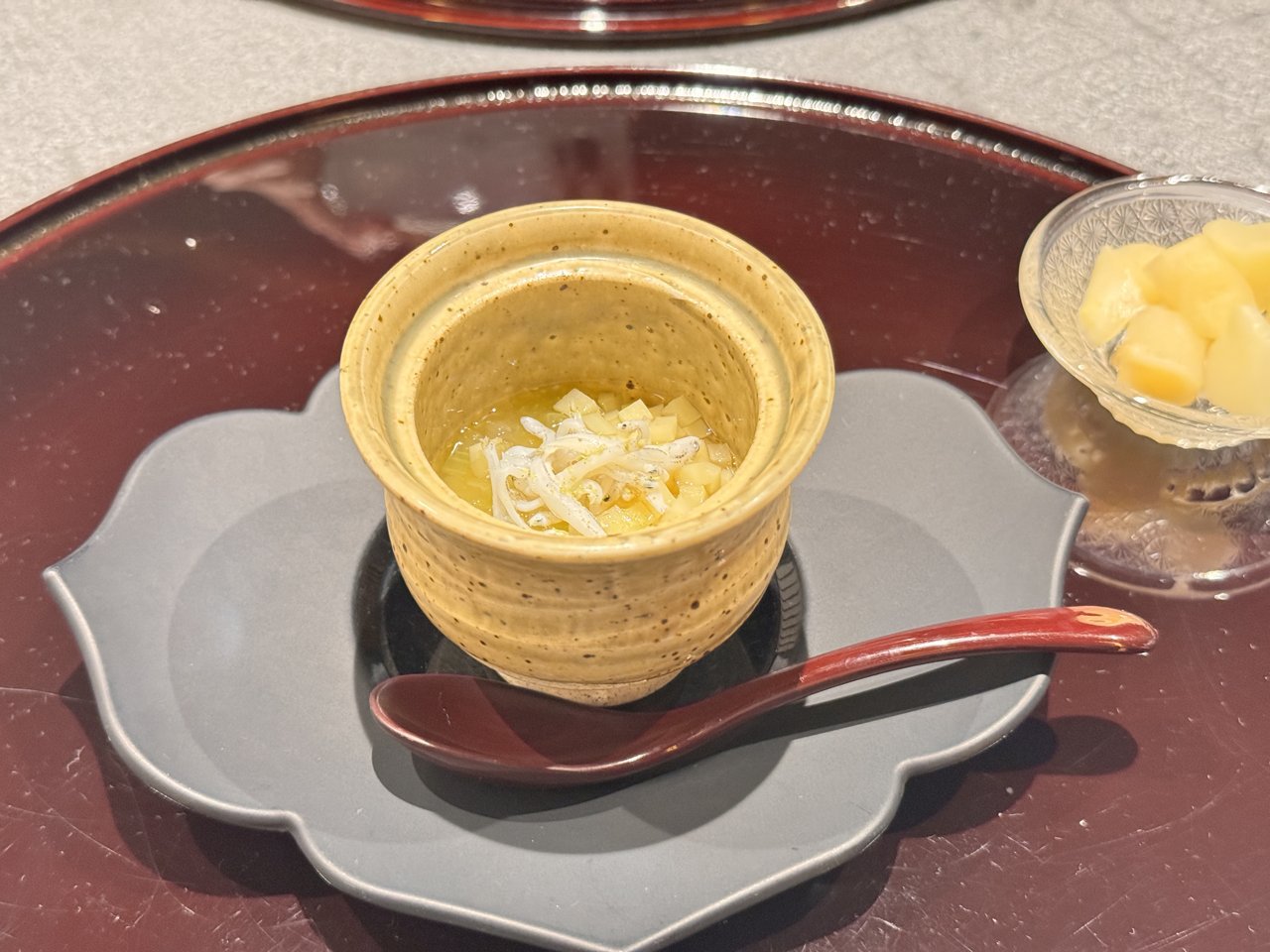 黄色い焼き物の器に入った椀物。小さな魚と角切りの具が浮かぶ