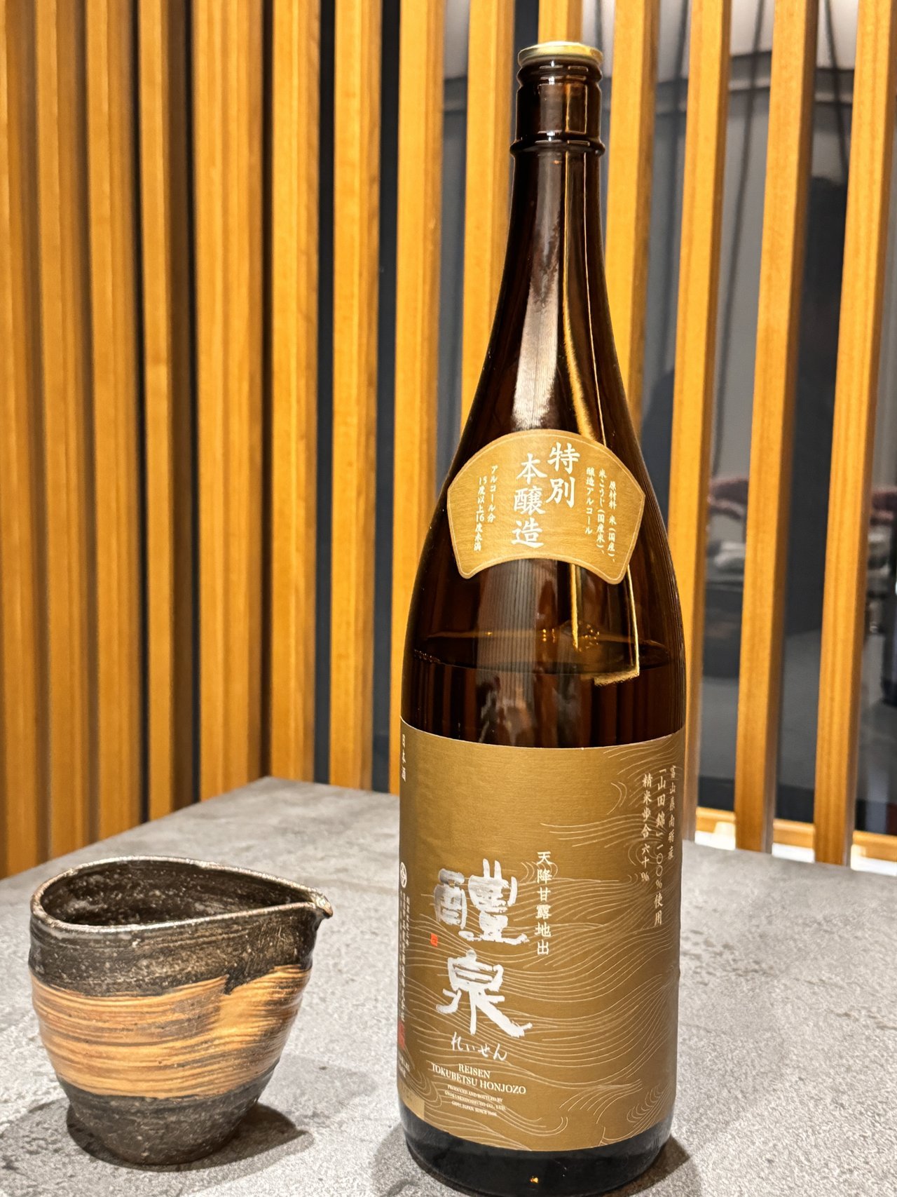 醴泉 特別本醸造の一升瓶と焼き物の片口。後ろに木の格子