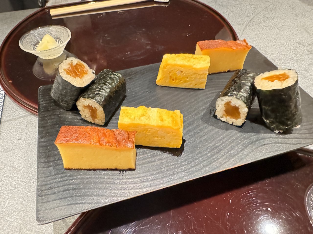 黒い板皿にのったカステラのような厚焼き玉子、だし巻きの玉子、干瓢巻き