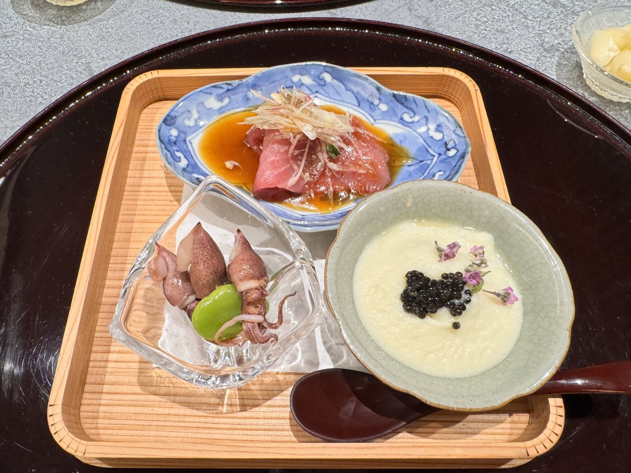 木の盆にのった前菜の3種盛り。たれをかけたマグロ、ホタルイカとそら豆、白いすり流しにキャビア