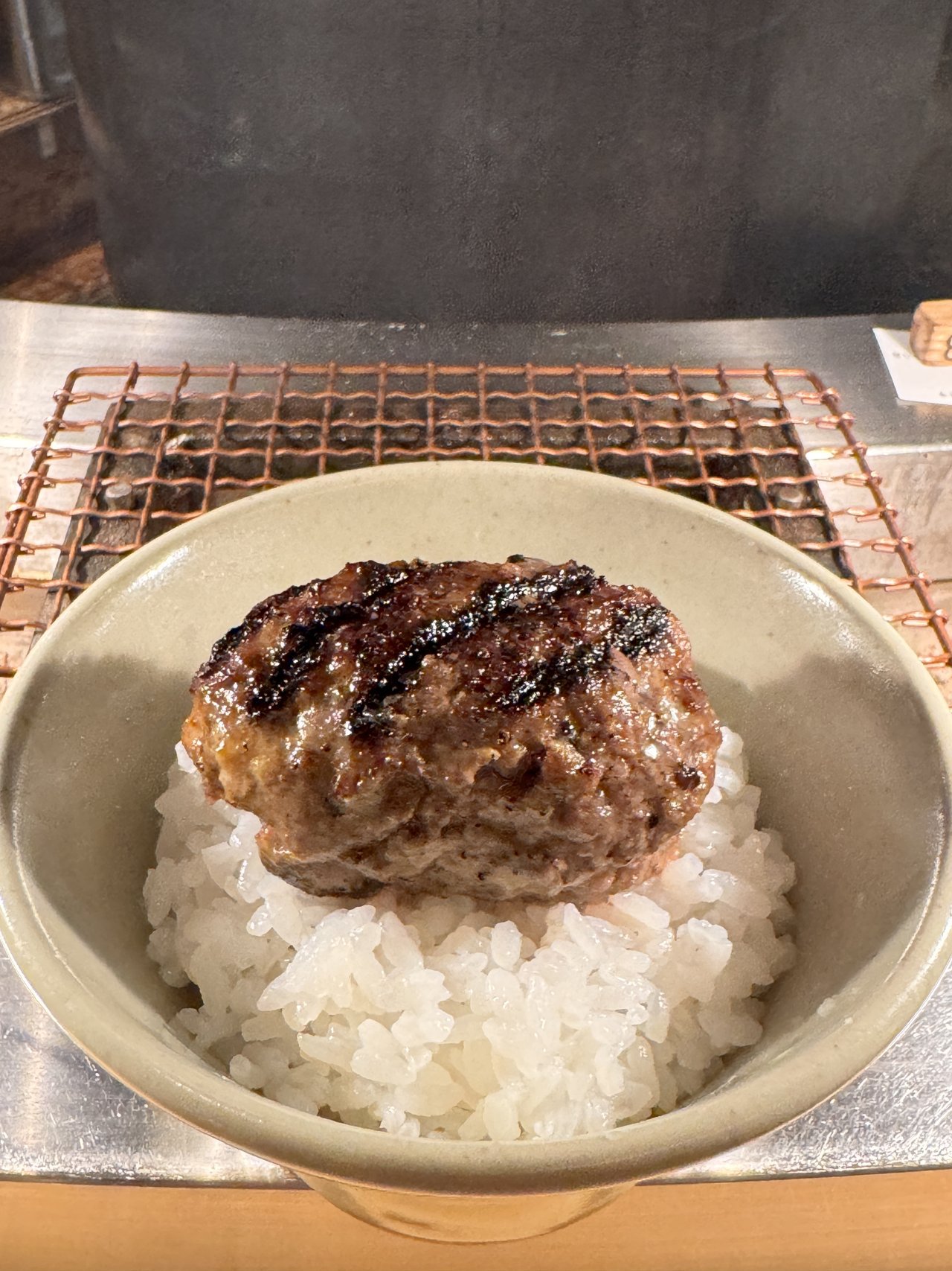 挽肉と米のハンバーグ。ごはんの上にのせた焼きたてのハンバーグと奥の銅の網