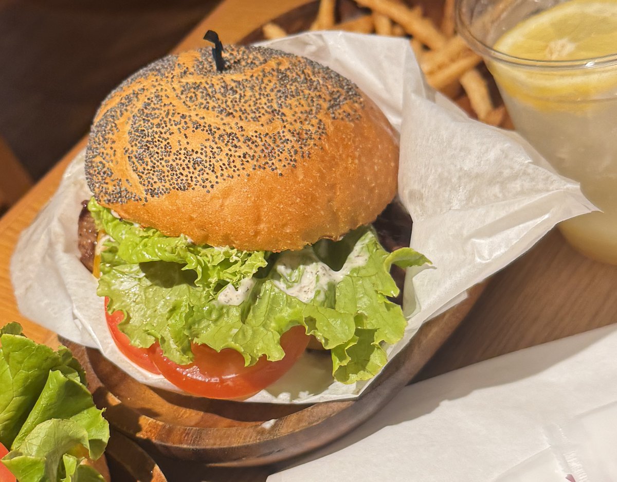 ポピーシードがびっしり付いたバンズのハンバーガー。レタスとトマトと白いソースを挟んで紙に包まれている