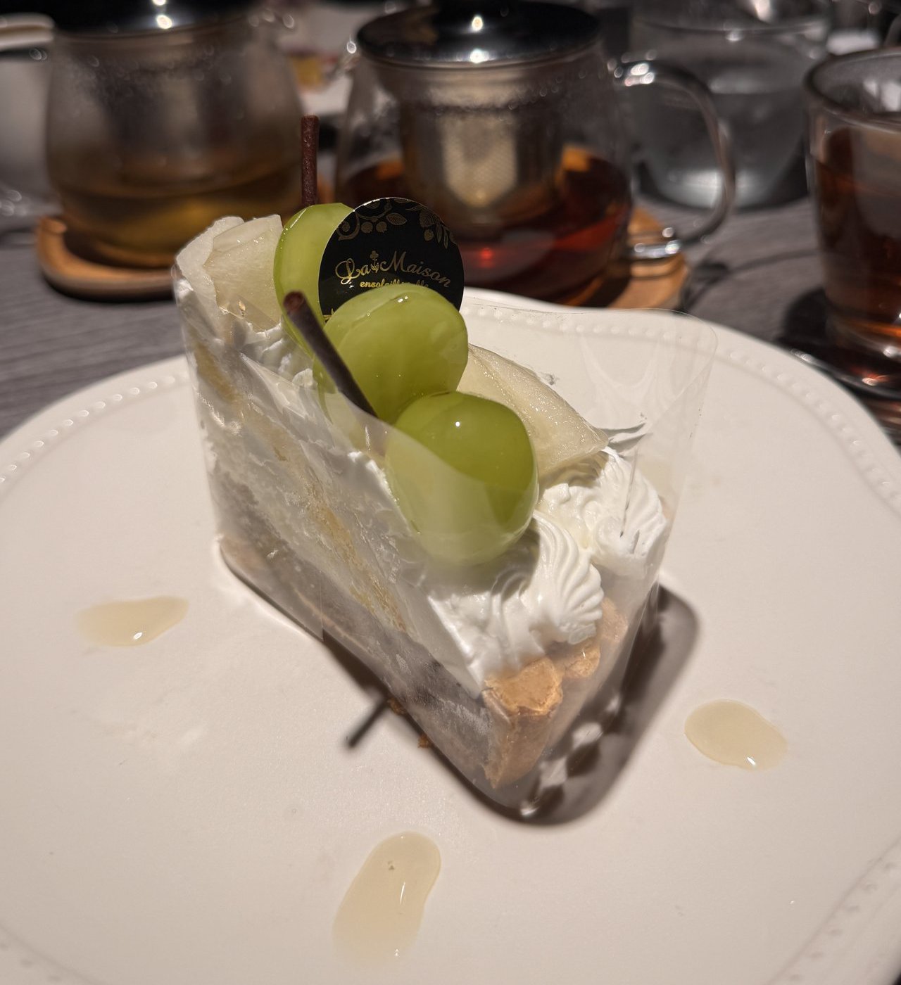 ケーキの奥に茶こし付きのガラスのティーポットとガラスのカップの紅茶
