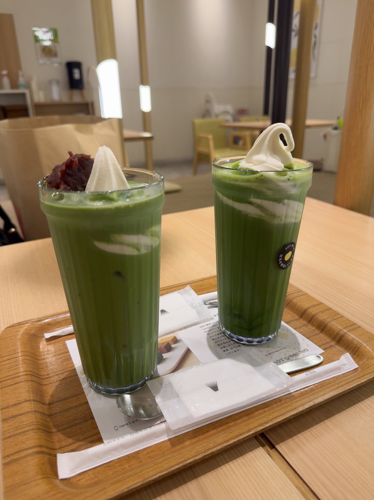 明るい木のテーブルの上に抹茶ラテ2杯のトレー。奥に黄緑のいすと木の柱が見える
