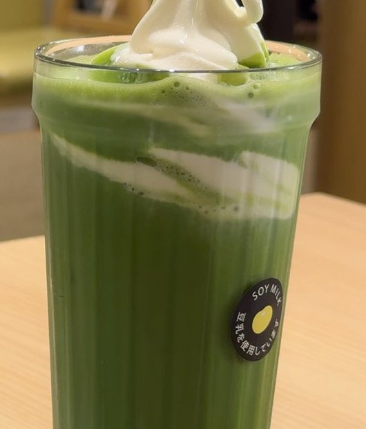 ソフトクリームがのった抹茶ラテのグラスに、SOY MILK 豆乳を使用しています と書かれた丸いシールが貼られている