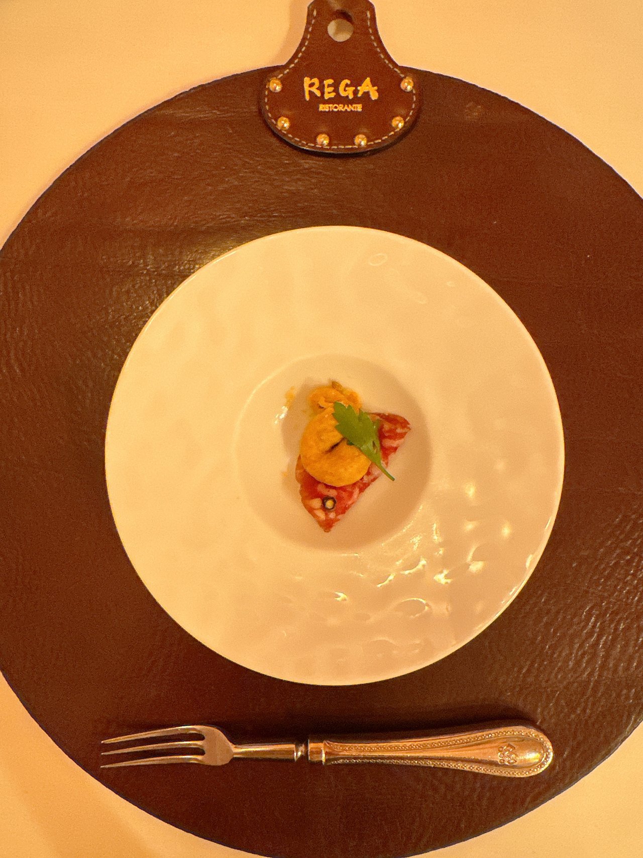 白い深皿の真ん中にのったサラミとオレンジ色の具の小さな前菜