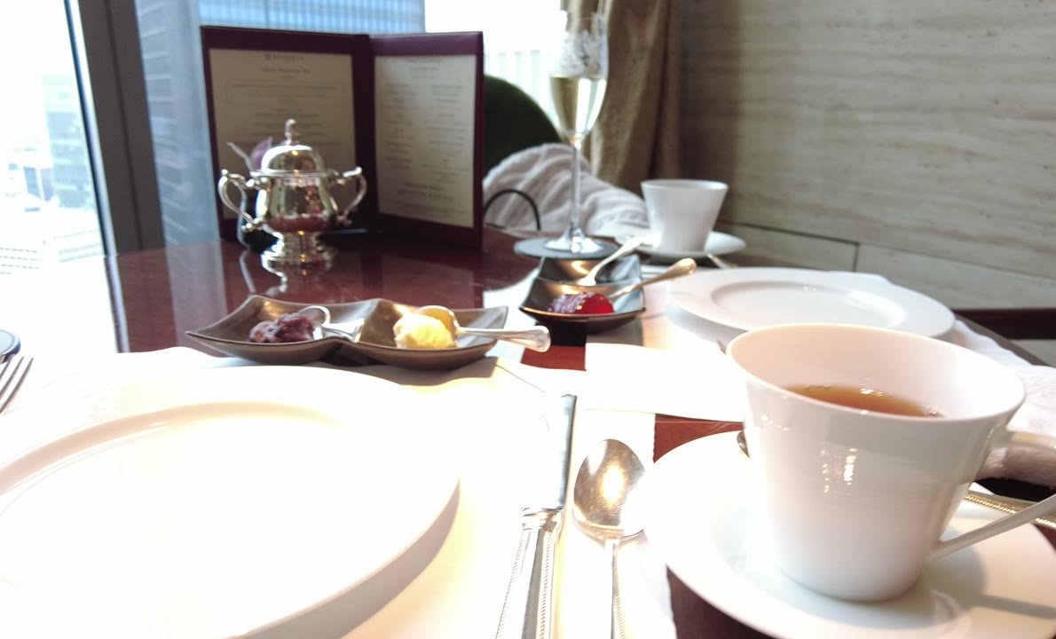 2つに分かれた小皿に小豆とクロテッドクリーム、別の小皿に赤いジャム。奥に銀のシュガーポットとメニュー冊子