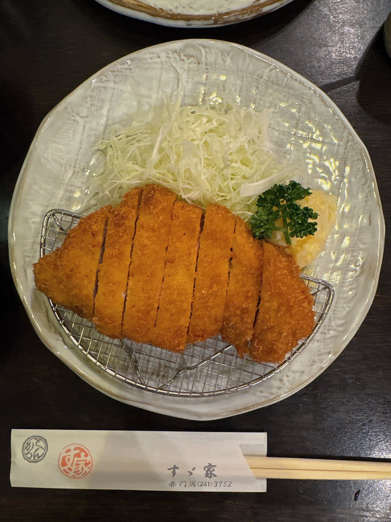 網の上で7切れに切られたすゞ家 赤門店の大きなとんかつと千切りキャベツ・ポテトサラダ・パセリ