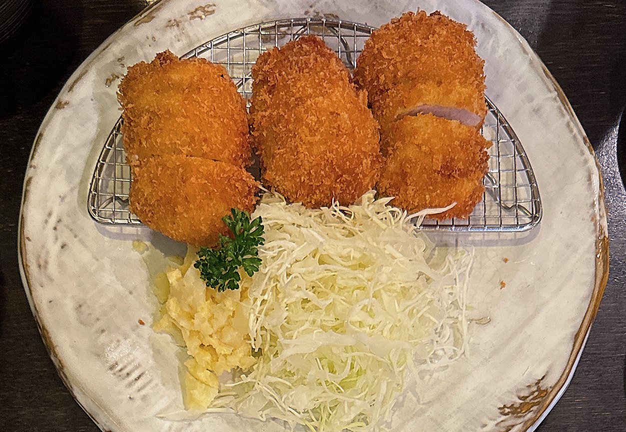 すゞ家 赤門店の丸いカツ3つ。網の上にのり千切りキャベツ・ポテトサラダ・パセリが付く