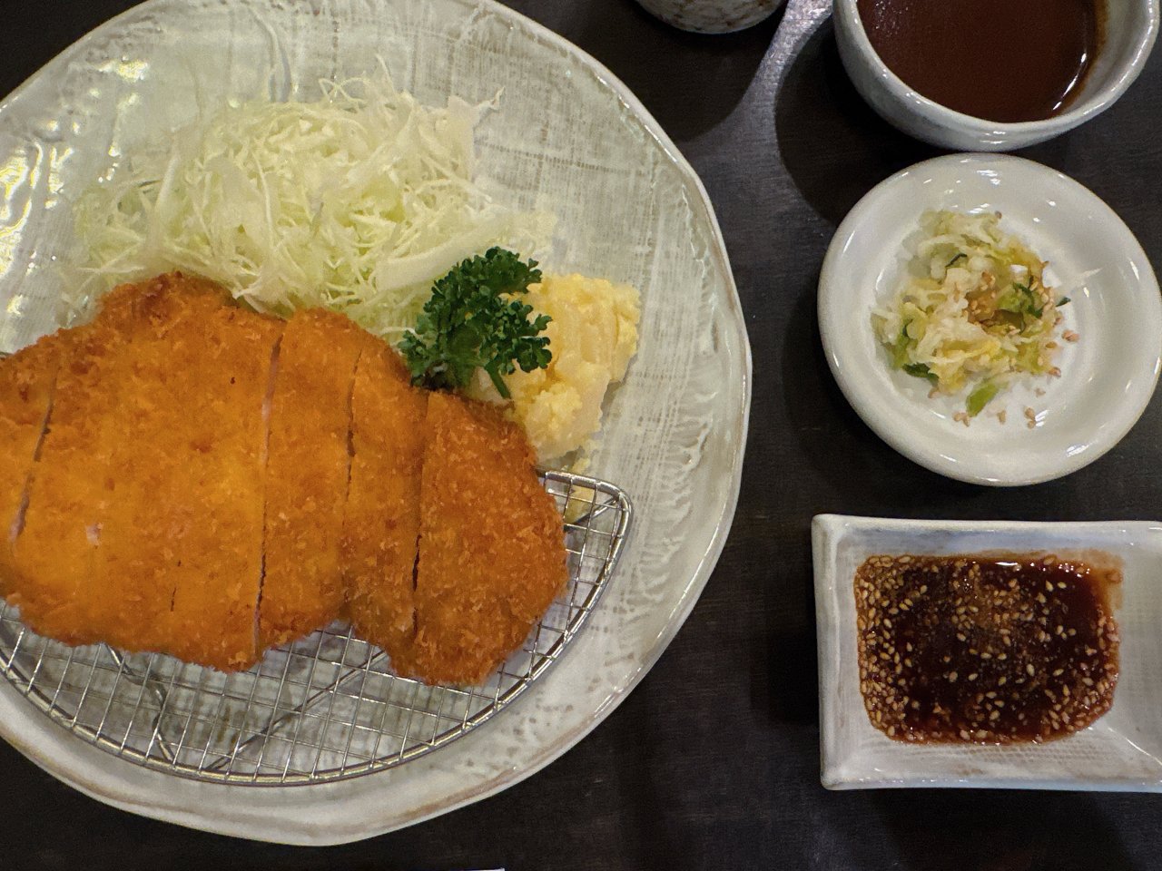 とんかつの横に並ぶソースの小鉢・漬物の小皿・ごまがたっぷり入ったたれの角皿