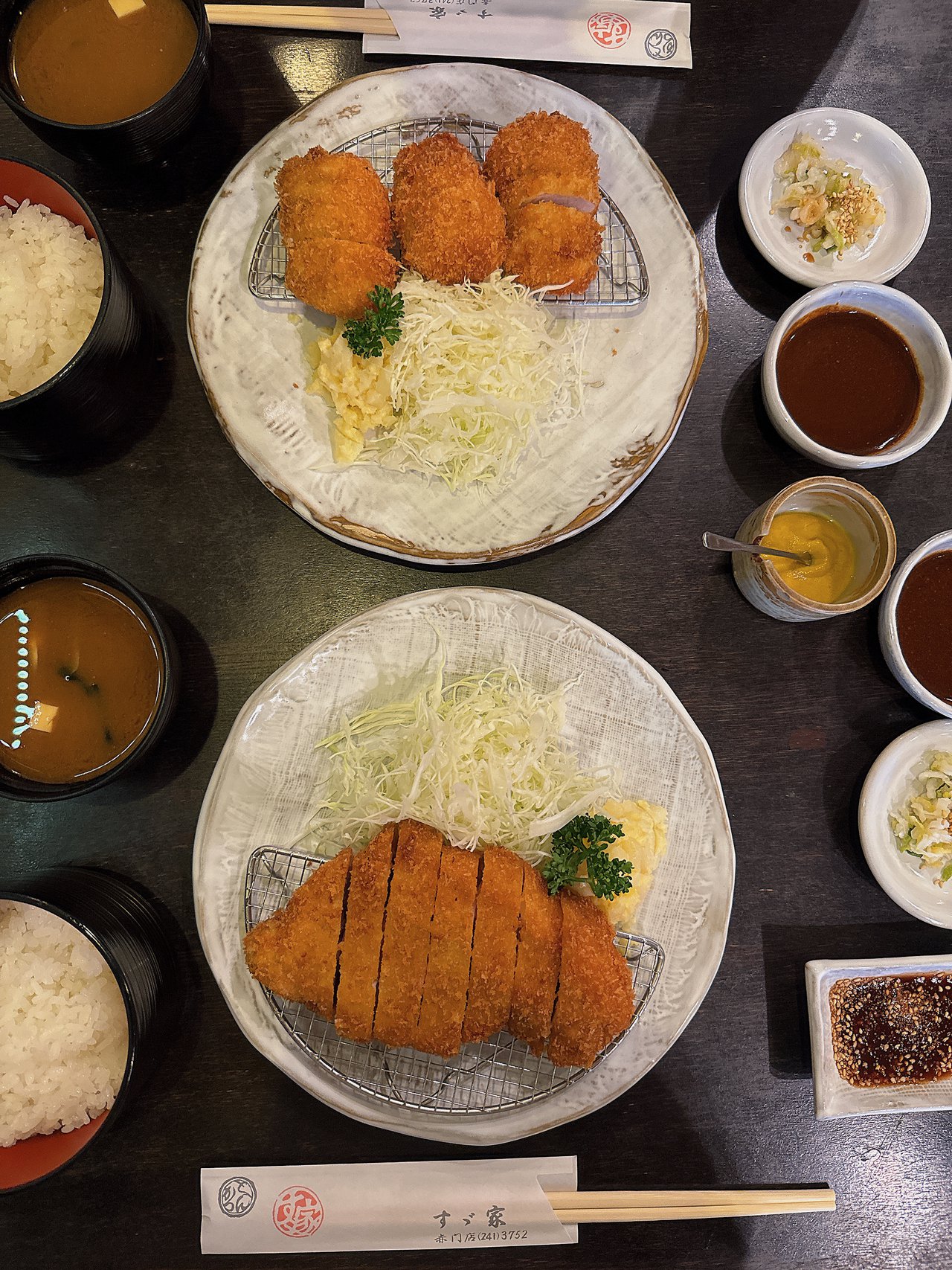 すゞ家 赤門店のとんかつ定食2人分を真上から撮った写真。大きなとんかつの皿と丸いカツの皿・ご飯と味噌汁・小皿のたれ